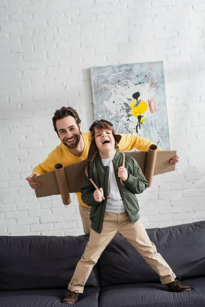 Homme heureux jouant avec son fils en costume d'aviateur sur le canapé — Photo de stock