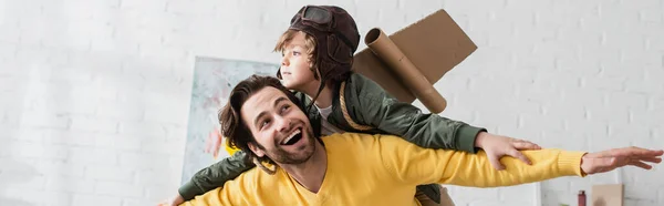 Niño en traje de aviador jugando con papá en casa, bandera - foto de stock