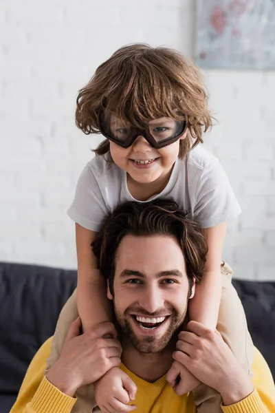 Smiling kid in aviator goggles hugging father — Stock Photo