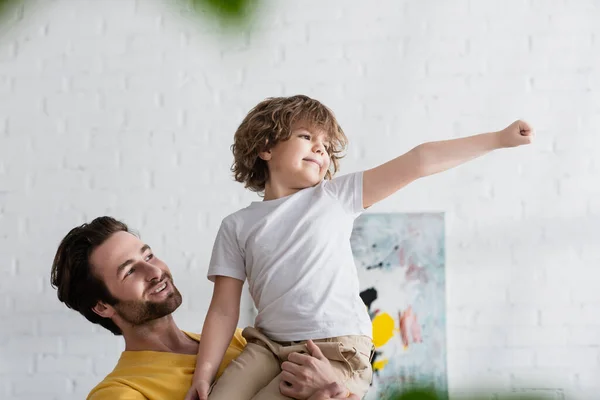 Hombre sosteniendo sonriente hijo haciendo gestos en casa - foto de stock