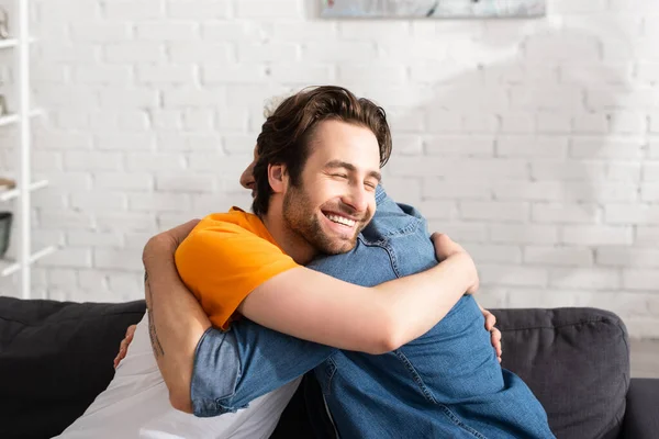 Homme souriant avec les yeux fermés embrassant père — Photo de stock