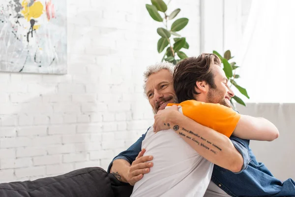 Улыбающийся мужчина обнимает сына на диване — стоковое фото