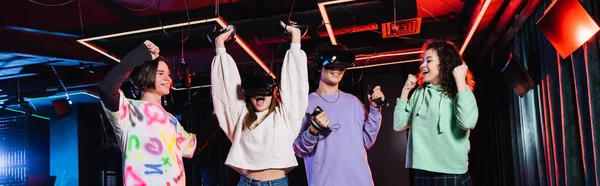 Взволнованные мультиэтнические подростки, показывающие победный жест в виртуальной игровой зоне, баннер — стоковое фото