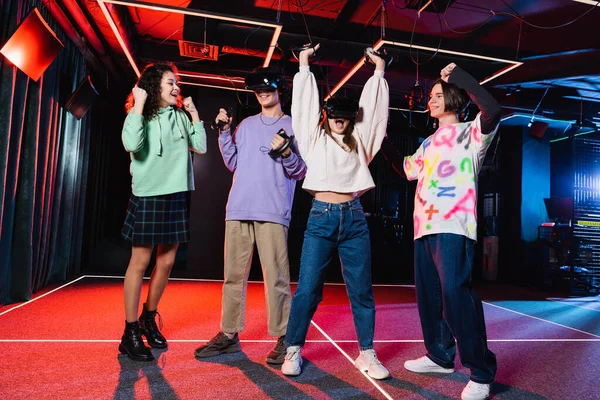 Веселі багатоетнічні підлітки показують радісний жест, розважаючись у ігровій кімнаті vr — стокове фото