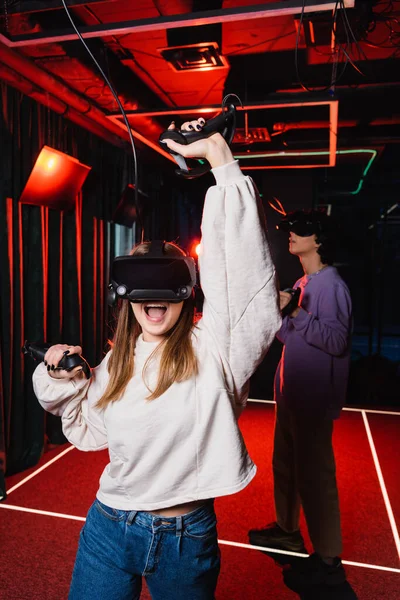 Excited girl showing rejoice gesture while gaming near blurred friend — Stock Photo