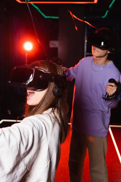 Astonished girl in headset gaming in vr play zone near blurred boy — Stock Photo