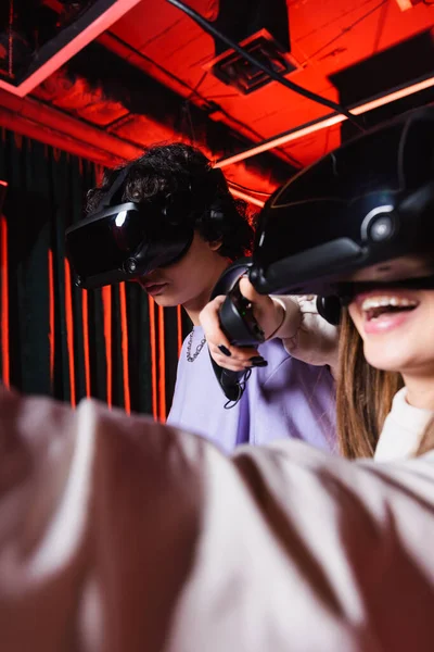 Alegre menina jogos no vr fone de ouvido perto adolescente menino, foreground borrado — Fotografia de Stock