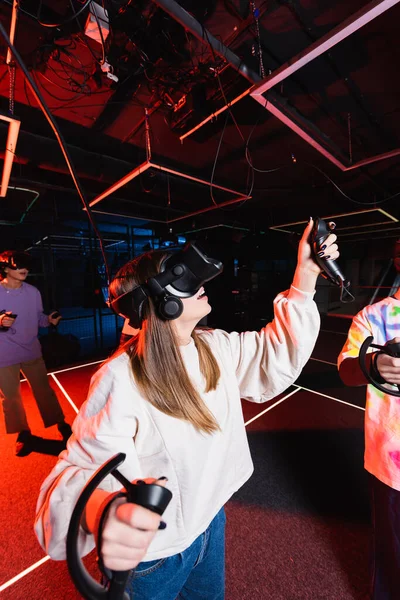 Adolescente ragazza che gioca in auricolare vr in sala giochi vicino agli amici — Foto stock