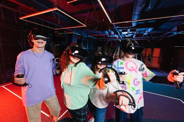 Happy multicultural teenagers in vr headsets having fun in game zone — Stock Photo