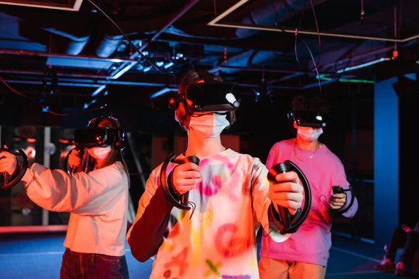 Teenage friends gaming in vr headsets and medical masks — Stock Photo