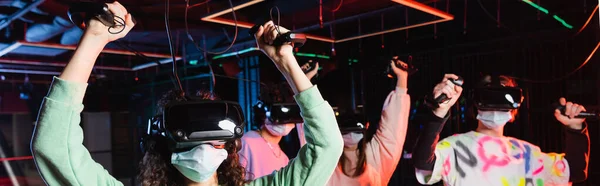 Excited interracial teenage friends showing win gesture in vr game room, banner — Stock Photo