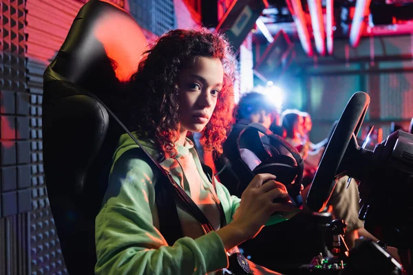 Chica afroamericana mirando a la cámara mientras está sentado con auriculares vr en simulador de coche - foto de stock