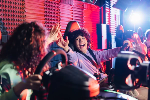 Excited boy giving high five to african american girl in car racing simulator — Stock Photo