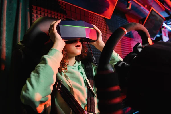 Astonished african american girl touching vr headset while playing on car racing simulator — Stock Photo