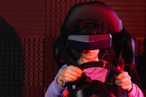 Teenage guy in virtual reality headset racing on car simulator — Stock Photo