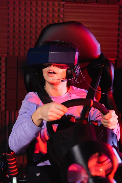 Astonished teenager in vr headset racing on car simulator — Stock Photo