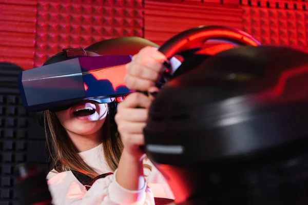 Erstaunt Teenager Mädchen Rennen in vr Headset auf Auto-Simulator, verschwommener Vordergrund — Stockfoto