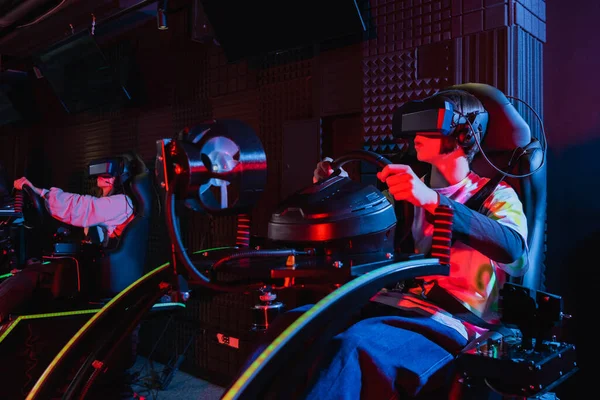 Teenagers in vr headsets racing on car simulators in game zone — Stock Photo