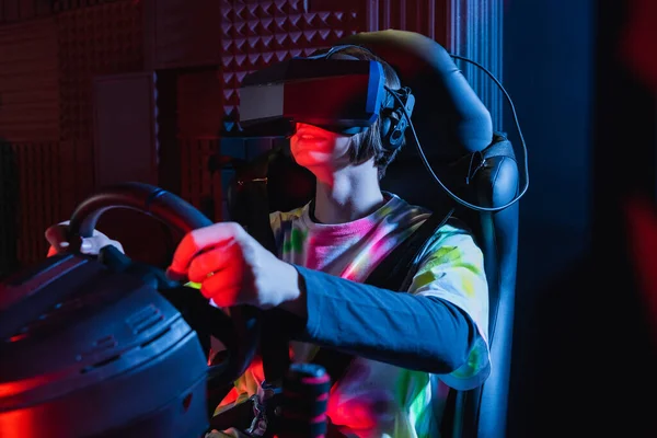 Happy teenage boy holding steering wheel while gaming on car simulator — Stock Photo