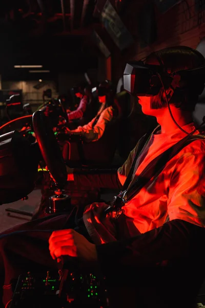 Teenager in vr headset racing on car simulator near blurred friends — Stock Photo