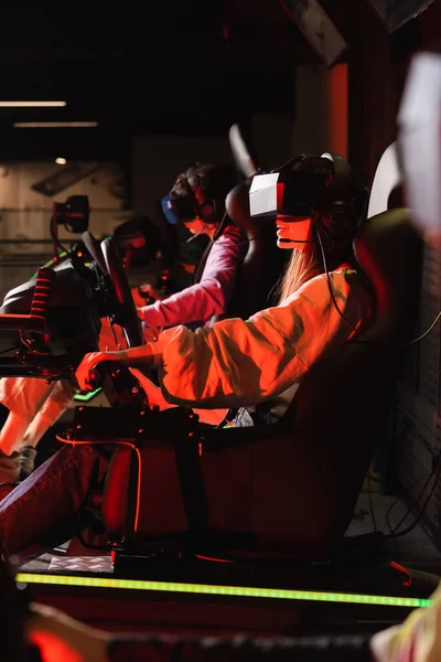 Teenage friends gaming on car racing simulators on blurred foreground — Stock Photo