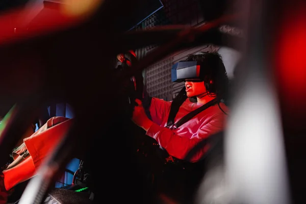 Excited guy in vr headset racing on car simulator, blurred foreground — Stock Photo