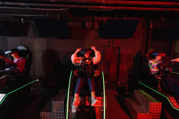 Изумленная девушка гонки в автомобиле симулятор вблизи геймеров в виртуальной игровой зоне — стоковое фото