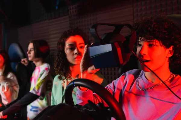 Adolescent étonné sur simulateur de voiture tenant casque vr près ami afro-américain — Photo de stock