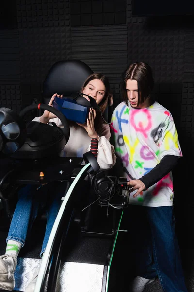 Teenage girl on car simulator holding vr headset near friend — Stock Photo