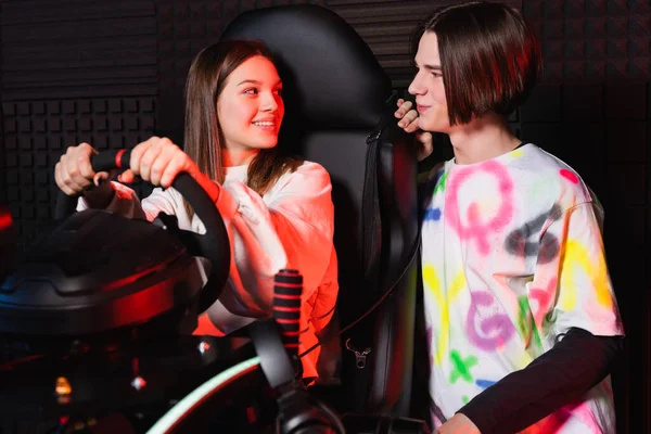 Amigos adolescentes sonriendo el uno al otro cerca de simulador de carreras de coches - foto de stock