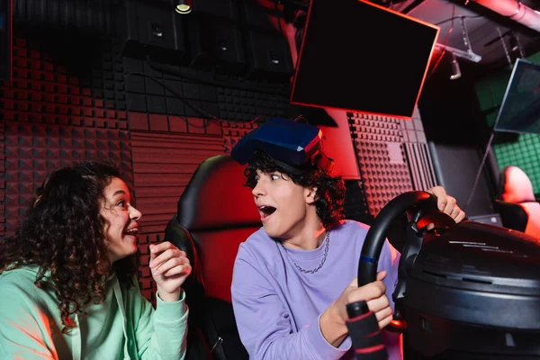 Amazed interracial friends looking at each other near car simulator — Stock Photo