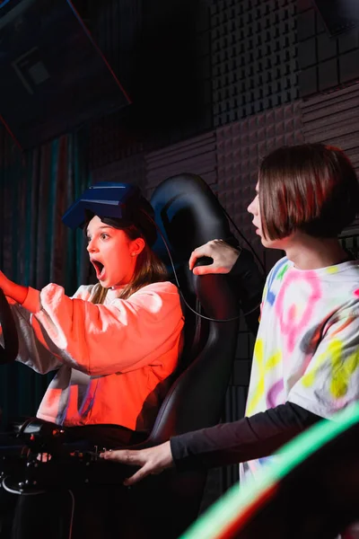 Menina surpreso gritando enquanto correndo no simulador de carro perto de amigo adolescente — Fotografia de Stock