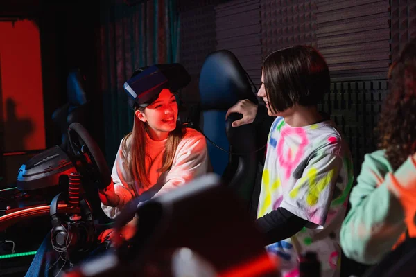 Adolescente hablando con chica sonriente en simulador de carreras de coches - foto de stock