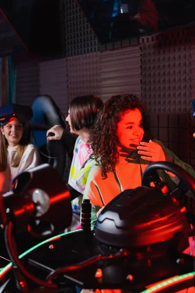 Alegre afroamericana chica cerca de amigos en coche carreras simuladores - foto de stock