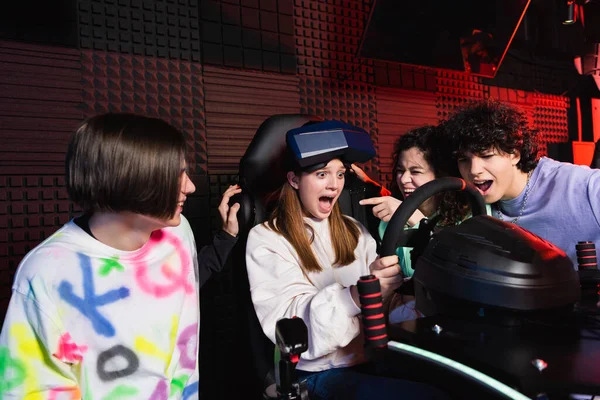 Frightened girl screaming in racing simulator near laughing multicultural friends — Stock Photo