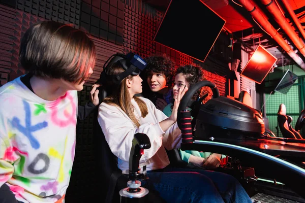 Взволнованные мультиэтнические друзья смотрят на девушку на автомобильном тренажере — стоковое фото