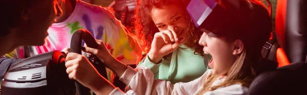 Adolescentes multiétnicos rindo perto de menina assustada no simulador de carro, banner — Fotografia de Stock