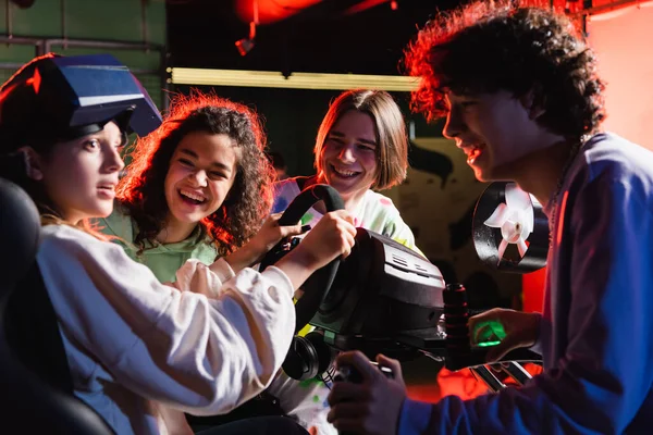 Cheerful multicultural friends laughing near scared girl in racing simulator — Stock Photo