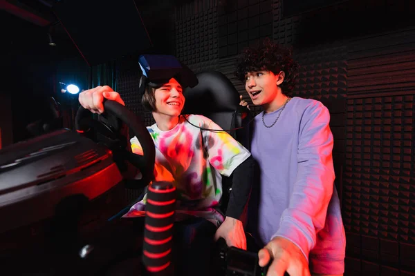 Excited boy talking to friend in car racing simulator — Stock Photo