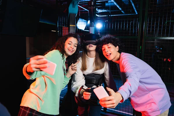 Happy interracial friends taking selfie with girl gaming in vr headset — Stock Photo