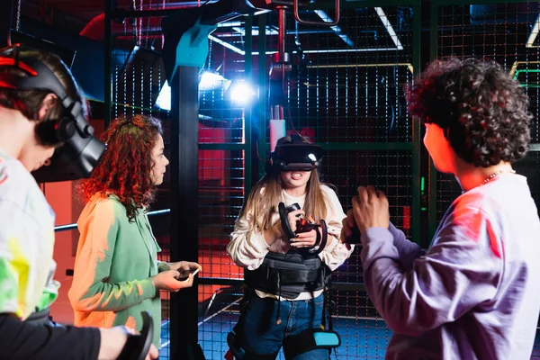 Возбужденная девочка-подросток игры в виртуальной гарнитуре рядом с многонациональными друзьями — стоковое фото