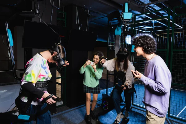 Alegre afroamericana chica tomando foto de amigos juego en vr auriculares - foto de stock