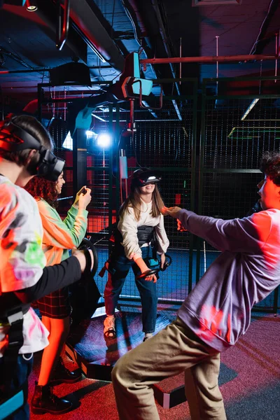 Smiling african american teenage girl taking photo of friends playing on vr platform — Stock Photo