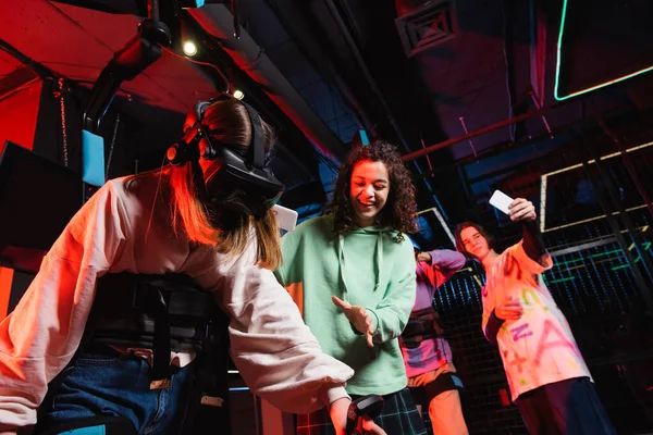 Cheerful interracial friends taking photo of girl gaming in vr headset — Stock Photo