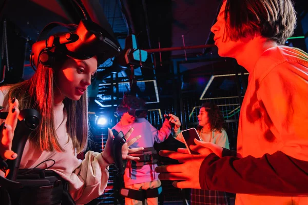 Adolescente menino segurando smartphone perto animado amigo gesticulando na zona de jogo vr — Fotografia de Stock