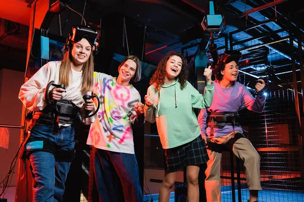 Cheerful multiethnic friends looking at camera while having fun in vr game room — Stock Photo