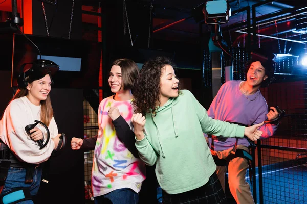 Cheerful interracial friends showing triumph gesture while having fun in vr play zone — Stock Photo