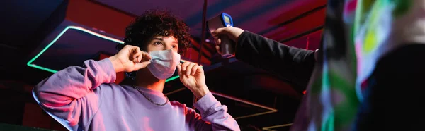 Jogador adolescente colocando máscara médica perto do controlador com pirômetro, banner — Fotografia de Stock