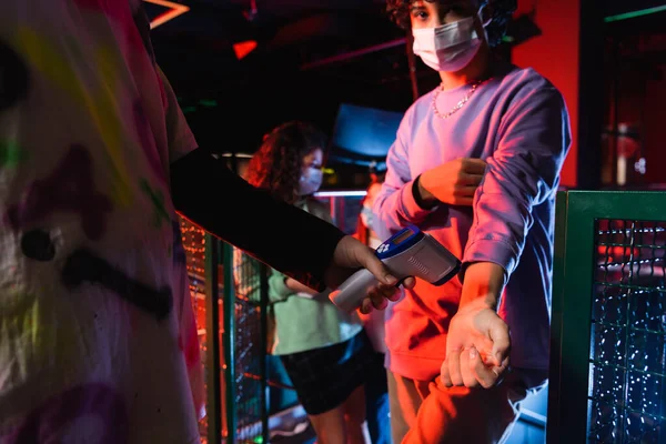 Controller measuring temperature of teenage boy in medical mask near girl on blurred background — Stock Photo