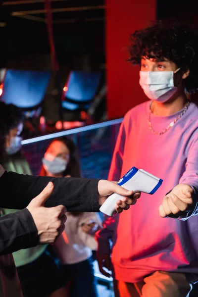 Contrôleur avec pyromètre montrant pouce vers le haut près garçon et les filles interracial floues dans des masques médicaux — Photo de stock